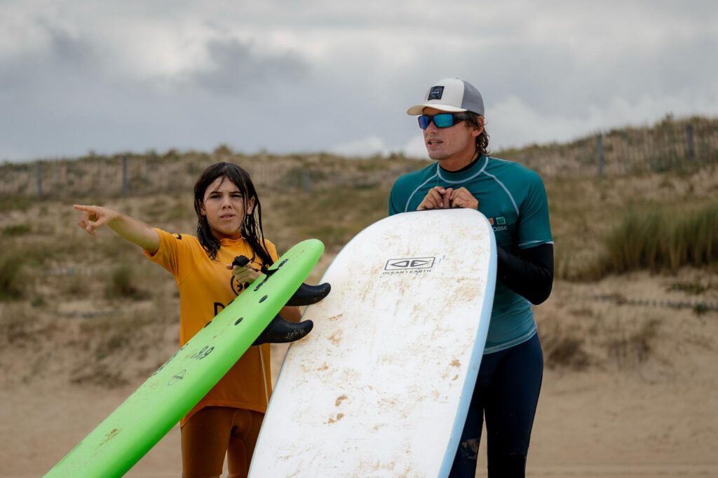Moniteur et jeune élève observant les vagues, planches en main