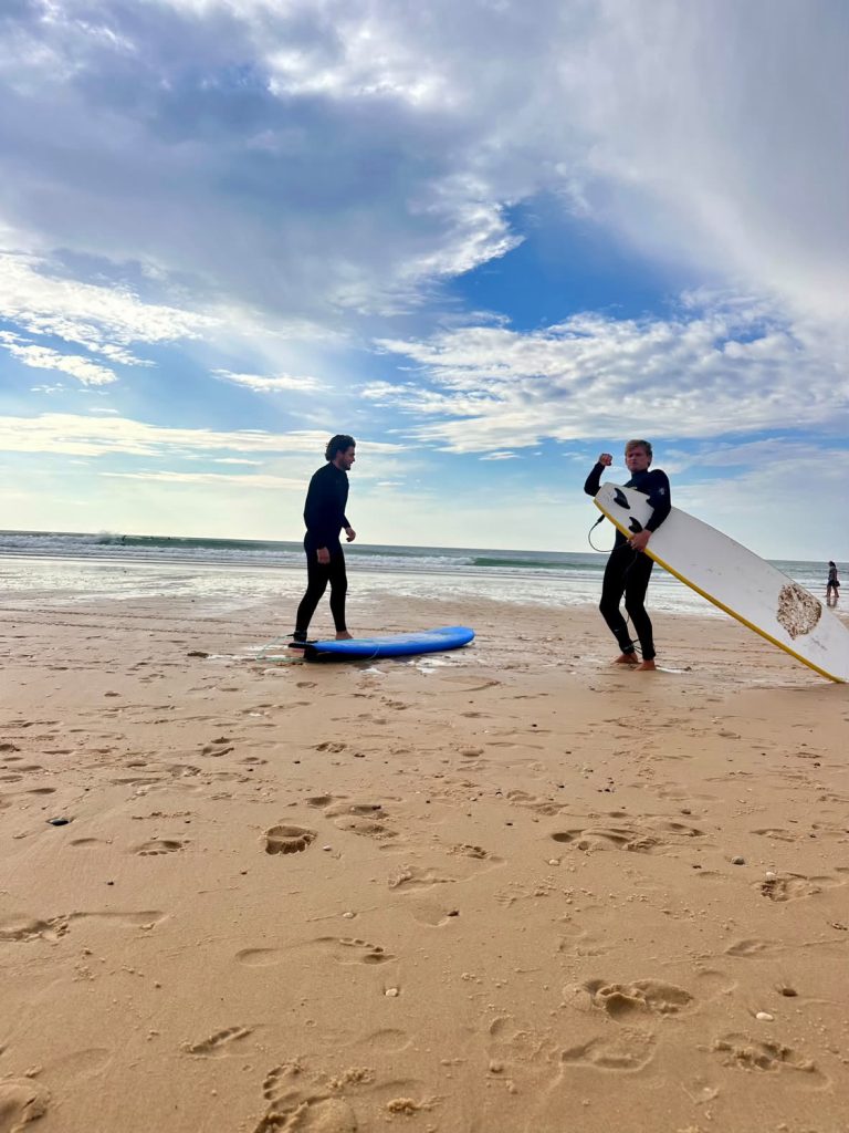 Deux surfeurs en combinaison sur la plage sous un ciel nuageux