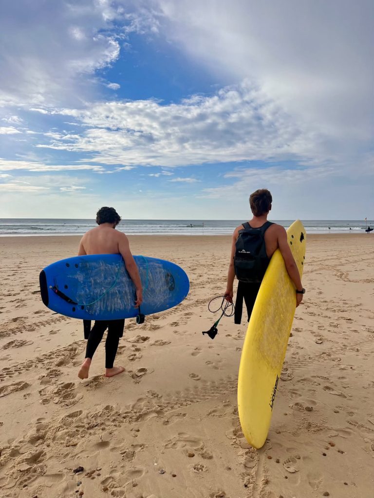Deux surfeurs marchant vers l’océan, planches sous le bras